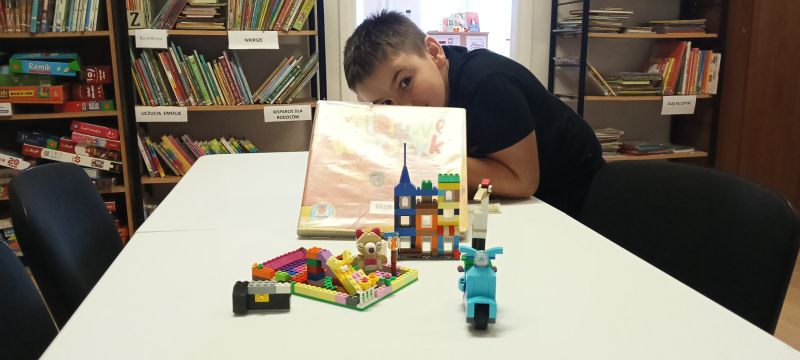Chłopiec prezentuje książkę Misiowe wierszyki oraz to co uczestnicy zajęć zbudowali z klocków lego na zajęciach