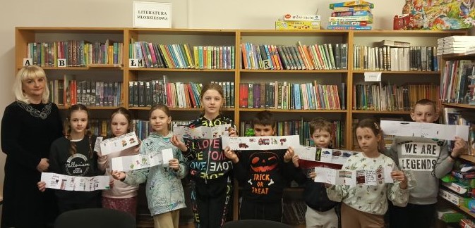 Uczniowie klasy III pozują do zdjęcia ze swoja książeczką leporello obok regałów z książkami 