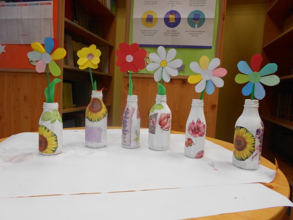 Na stoliku w bibliotece ustawione wazoniki ozdobione na zajęciach, w nich kwiatki również wykonane na zajęciach