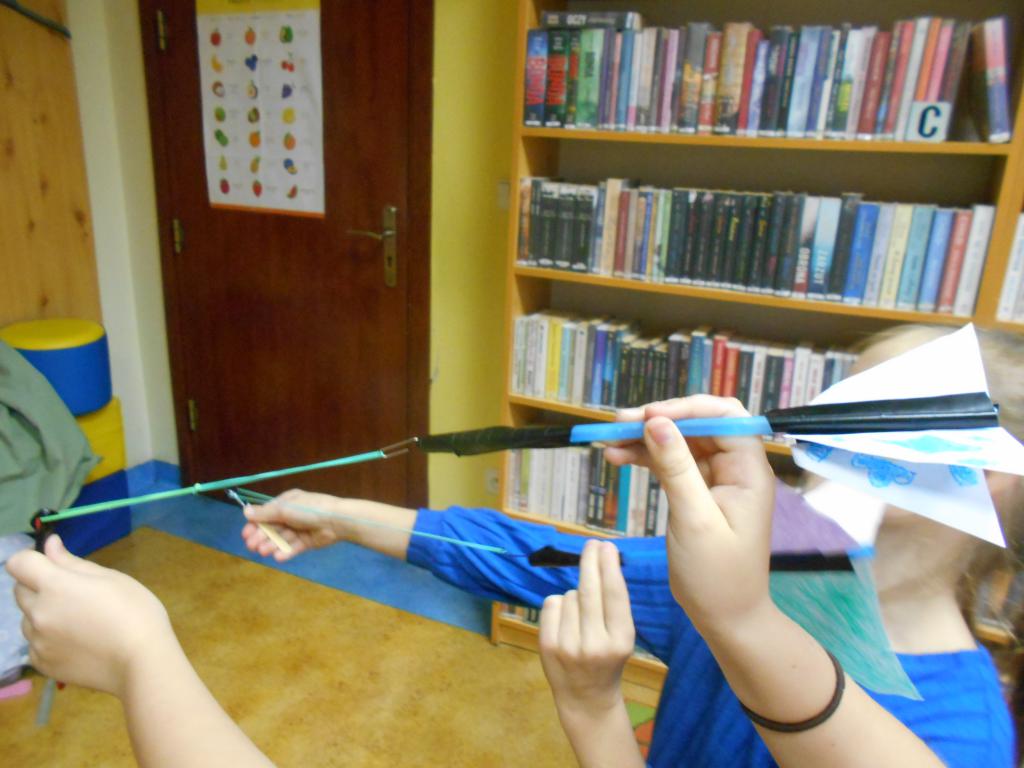 Dwie dziewczynki - uczestniczki zajęć bibliotecznych - naciągają gumki na swoich rakietach, aby z nich wystrzelić