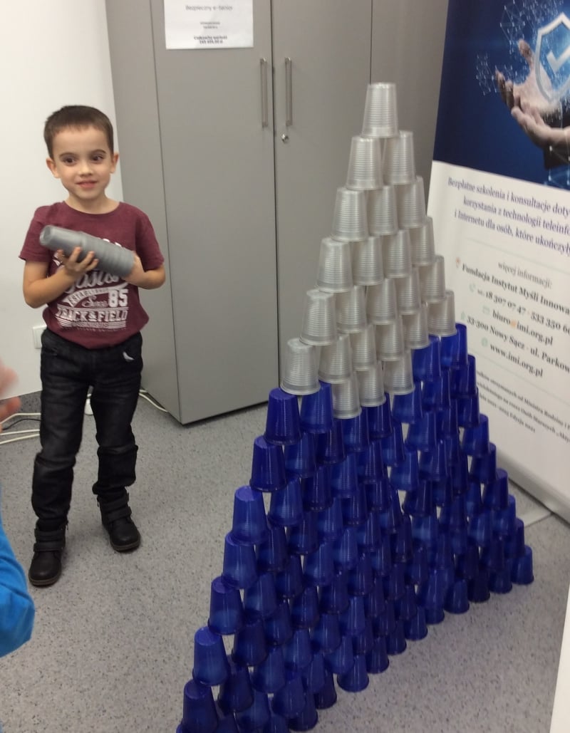 Chłopiec stoi koło wieży z kubeczków