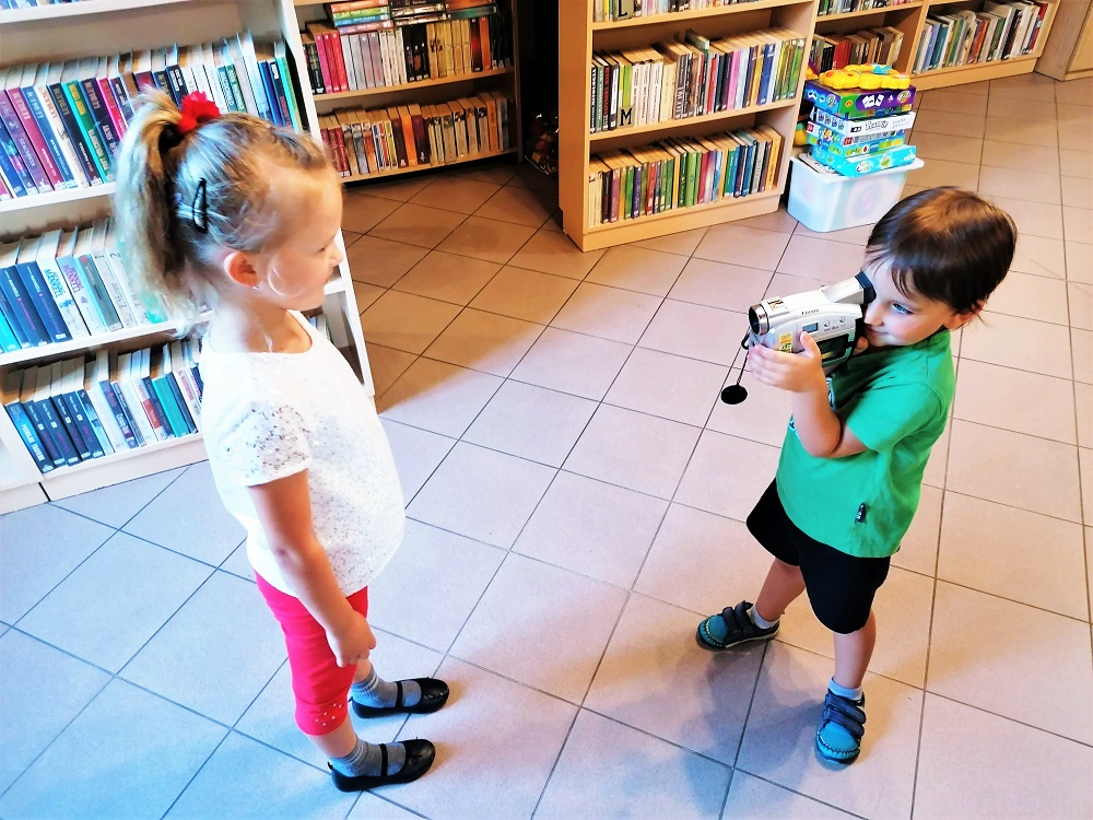 Chłopczyk i dziewczynka bawią się minikamerą dla dzieci. Chłopczyk obserwuje przez kamerę otoczenie
