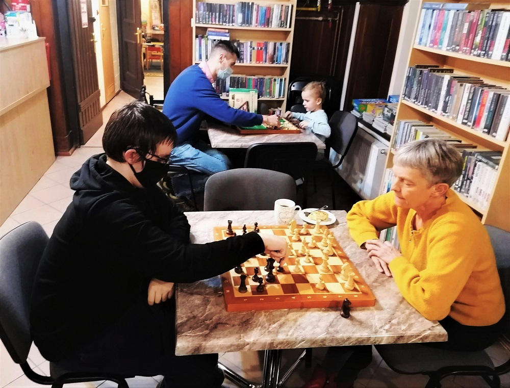 Przy stolikach rozgrywane są partie szachowe.