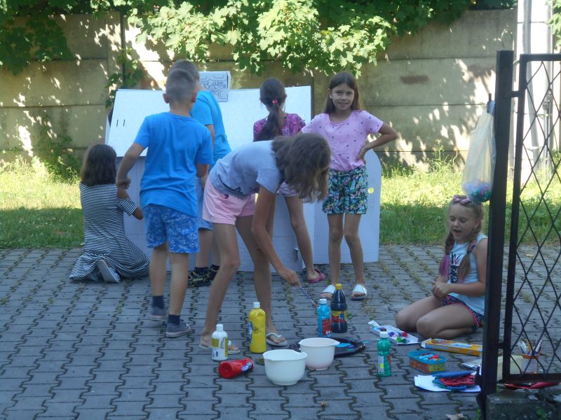 Dzieci malują farbami kwiaty na tekturowym domku
