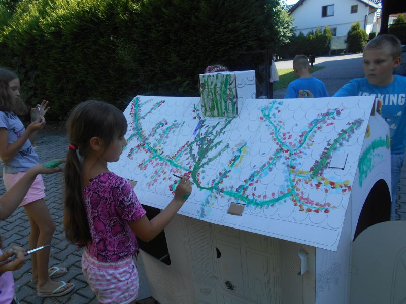 Dzieci ozdabiają dach kartonowego domku kwiatami