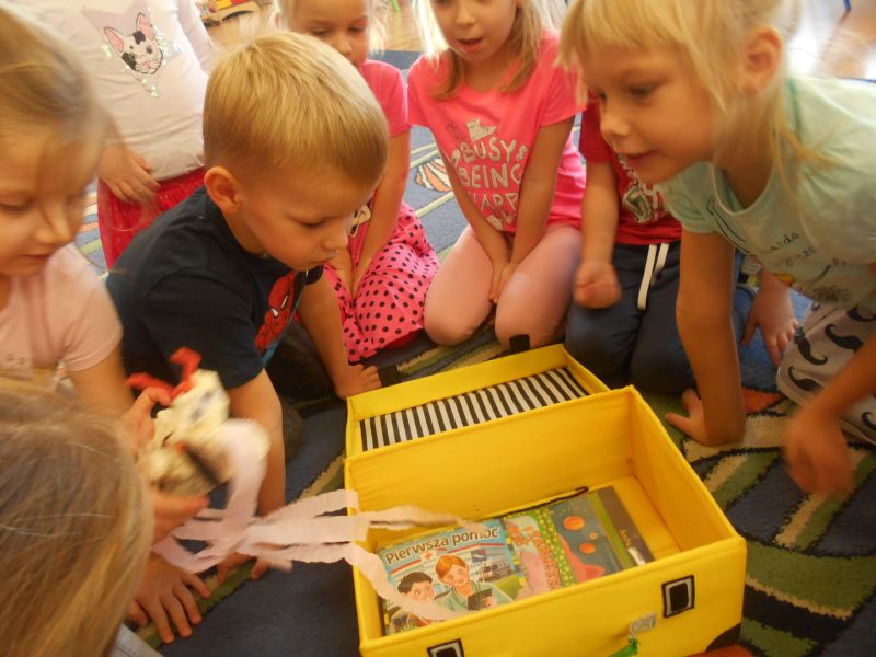 Dzieci zaglądają do żółtego kuferka bibliotecznego szukając skarbów książkowych