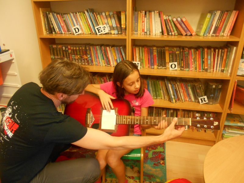Lekcja gry na gitarze - Pan Piotr pokazuje jak się gra na gitarze jednej z uczestniczek zajęć bibliotecznych 