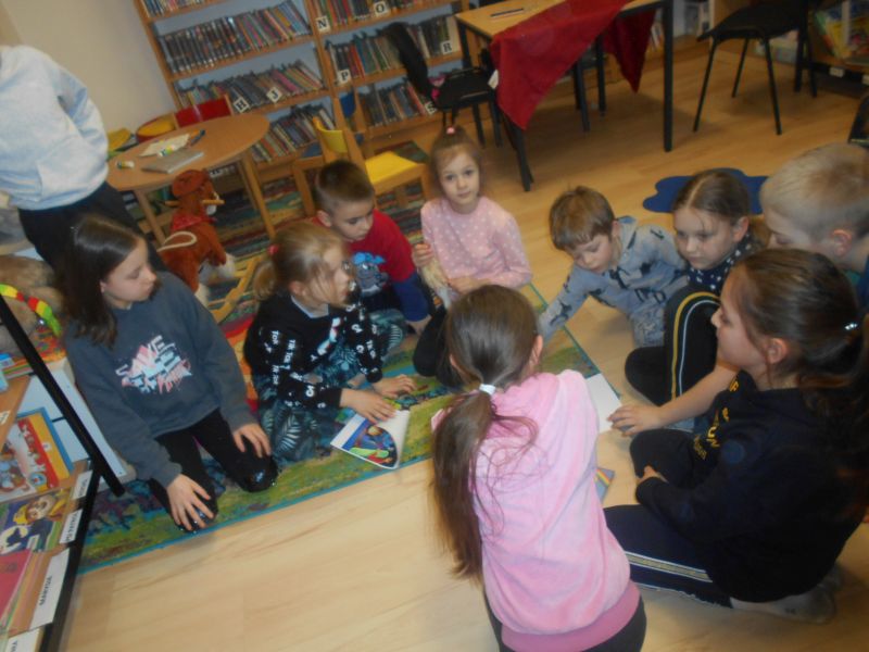 Uczestnicy zajęć rozwiązują zagadki siedząc w grupach na podłodze