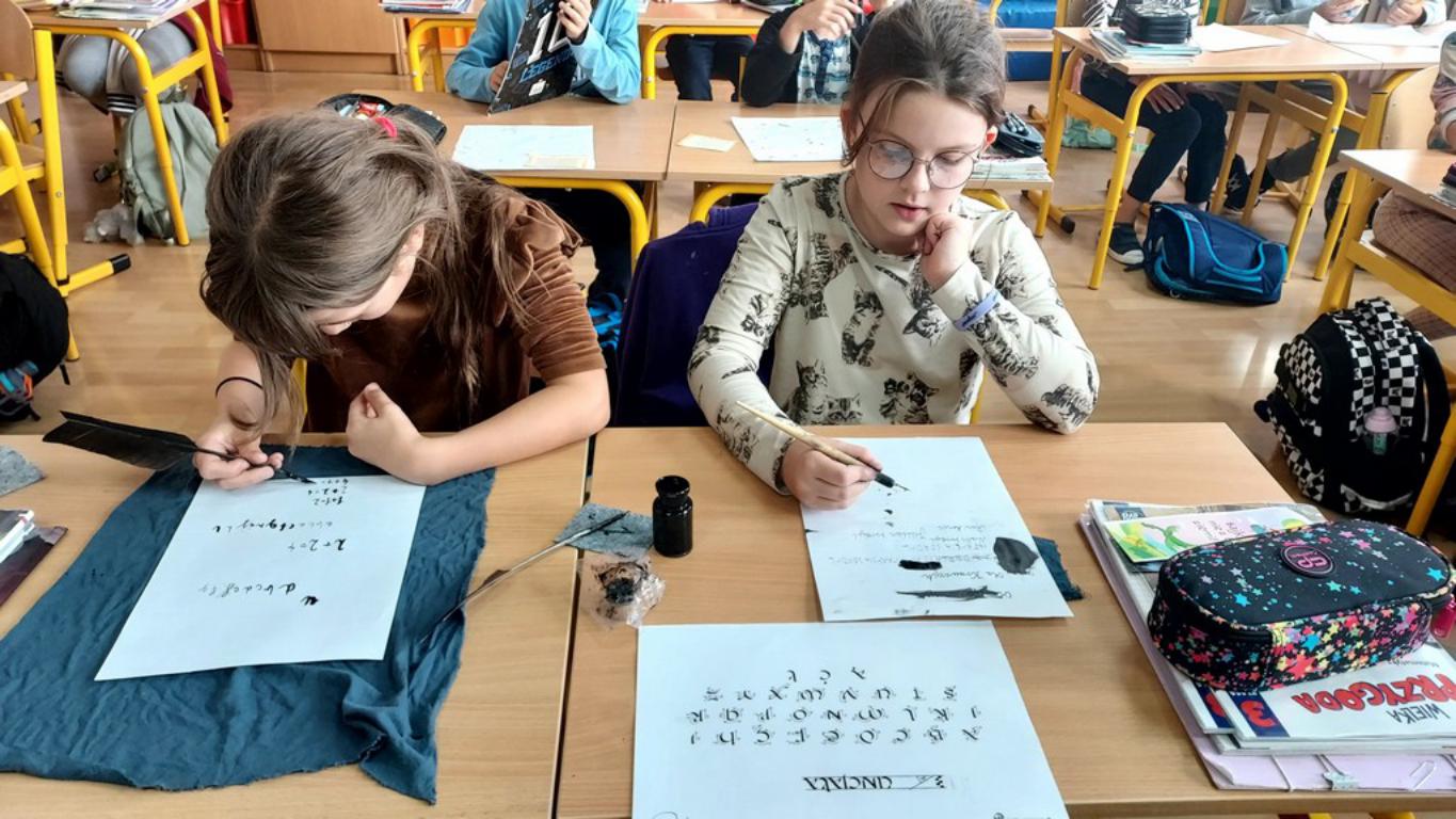 Dwie uczennice ćwiczą pismo kaligraficzne prawdziwymi piórami