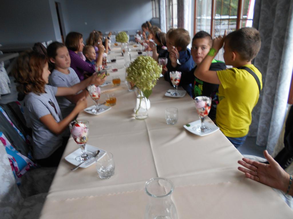 Dzieci siedzą przy stoliku i zajadają słodki deser lodowy.